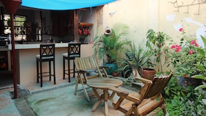 Un patio con sillas y mesa de madera, rodeado de plantas en macetas y un dosel azul.