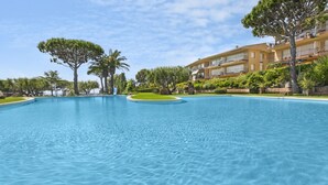 A large, clear swimming pool with a curved design, surrounded by lush greenery and a multi-story building with balconies. - ILLA 76 -Nice apartment with sea views, pool and near the beach of Calella (Calella de Palafrugell)