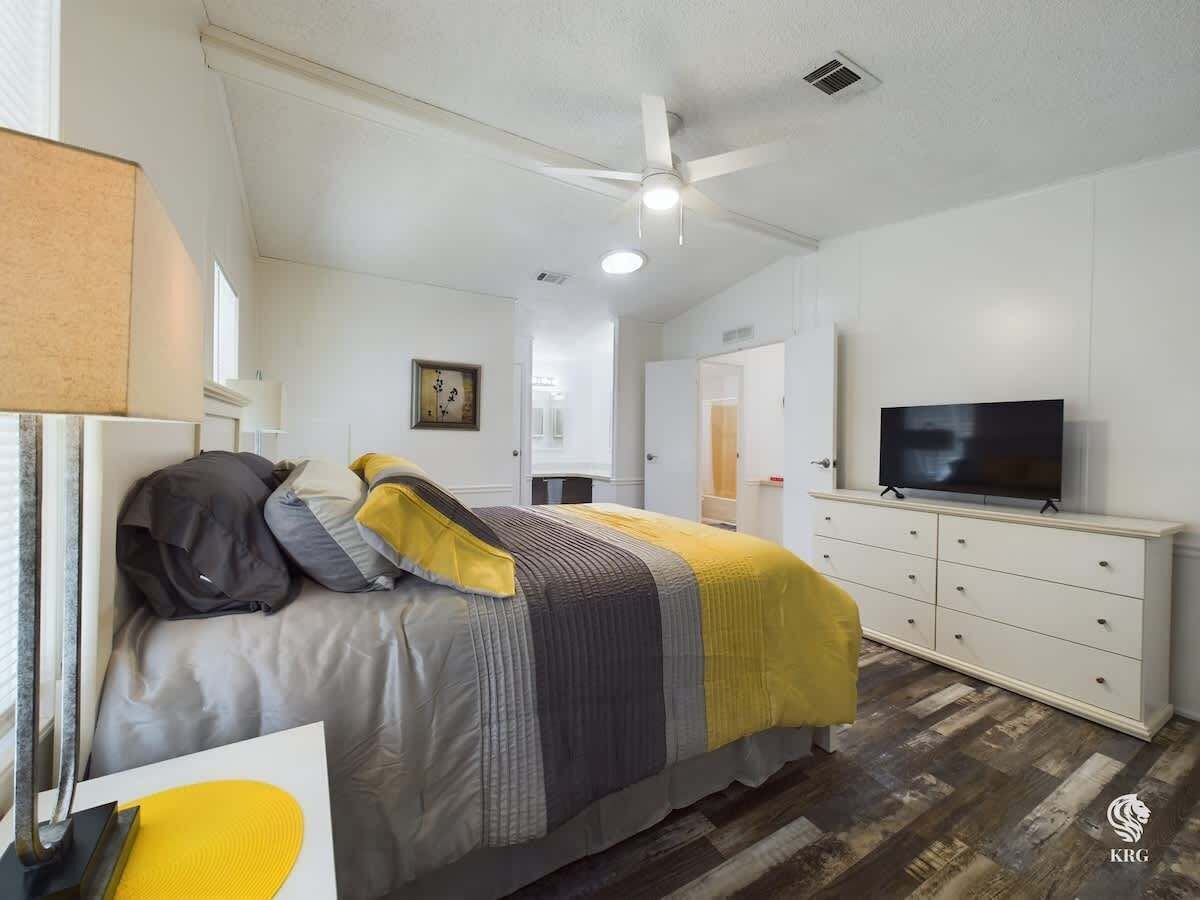 Une chambre à coucher avec un lit, une télévision, une commode et un ventilateur de plafond.