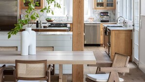 Una cocina moderna con vigas de madera, una isla central y un comedor con sillas de ratán.