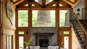 Un salón amplio con chimenea de piedra, mobiliario blanco y techo de madera.