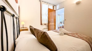 A hotel room with a bed, a nightstand with a lamp, a wooden door, and a view of the dining area. - El racó de Montana Park (Enveitg)