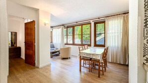 A dining area with a wooden table and chairs, a sofa, and a window with curtains. - El racó de Montana Park (Enveitg)