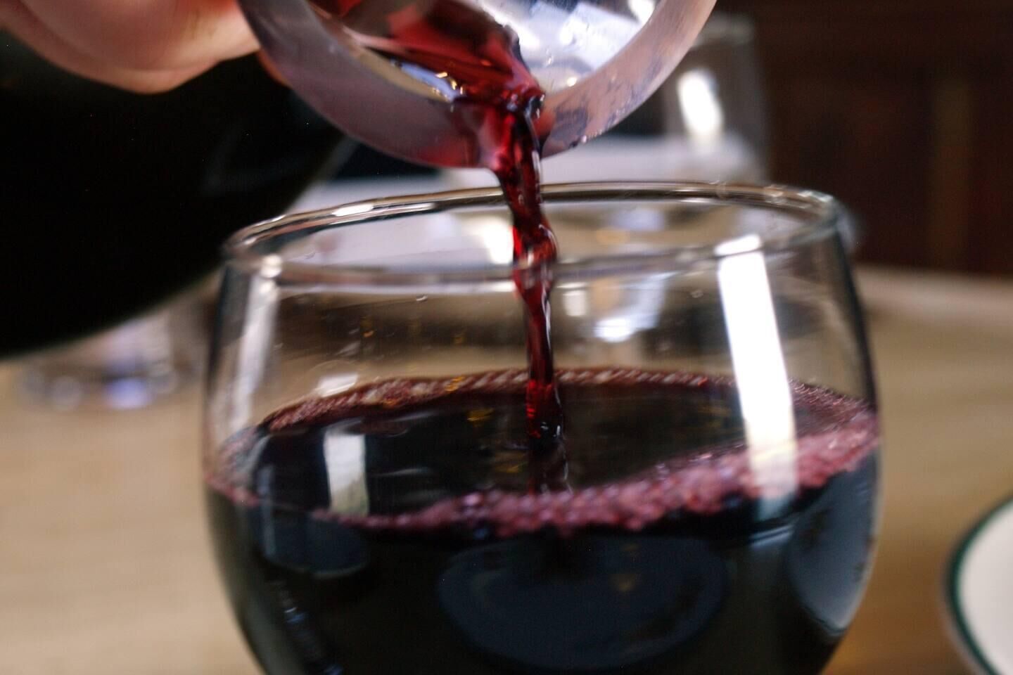 A hand pouring red liquid into a clear glass.
