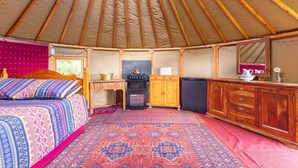 A yurt interior with a bed, kitchenette, and wooden cabinets.