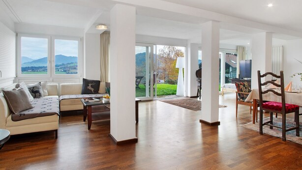 Amplia sala de estar con un conjunto de sofás, una mesa de comedor con sillas y ventanas grandes que ofrecen vistas al exterior.