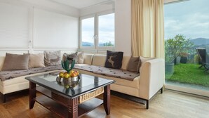 Una sala de estar con sofá, una mesa de centro con fruta y vistas al exterior.