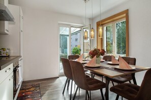 Eine moderne Küche mit weißen Schränken, ein Essbereich mit braunen Stühlen und ein großes Fenster mit Blick nach draußen.
