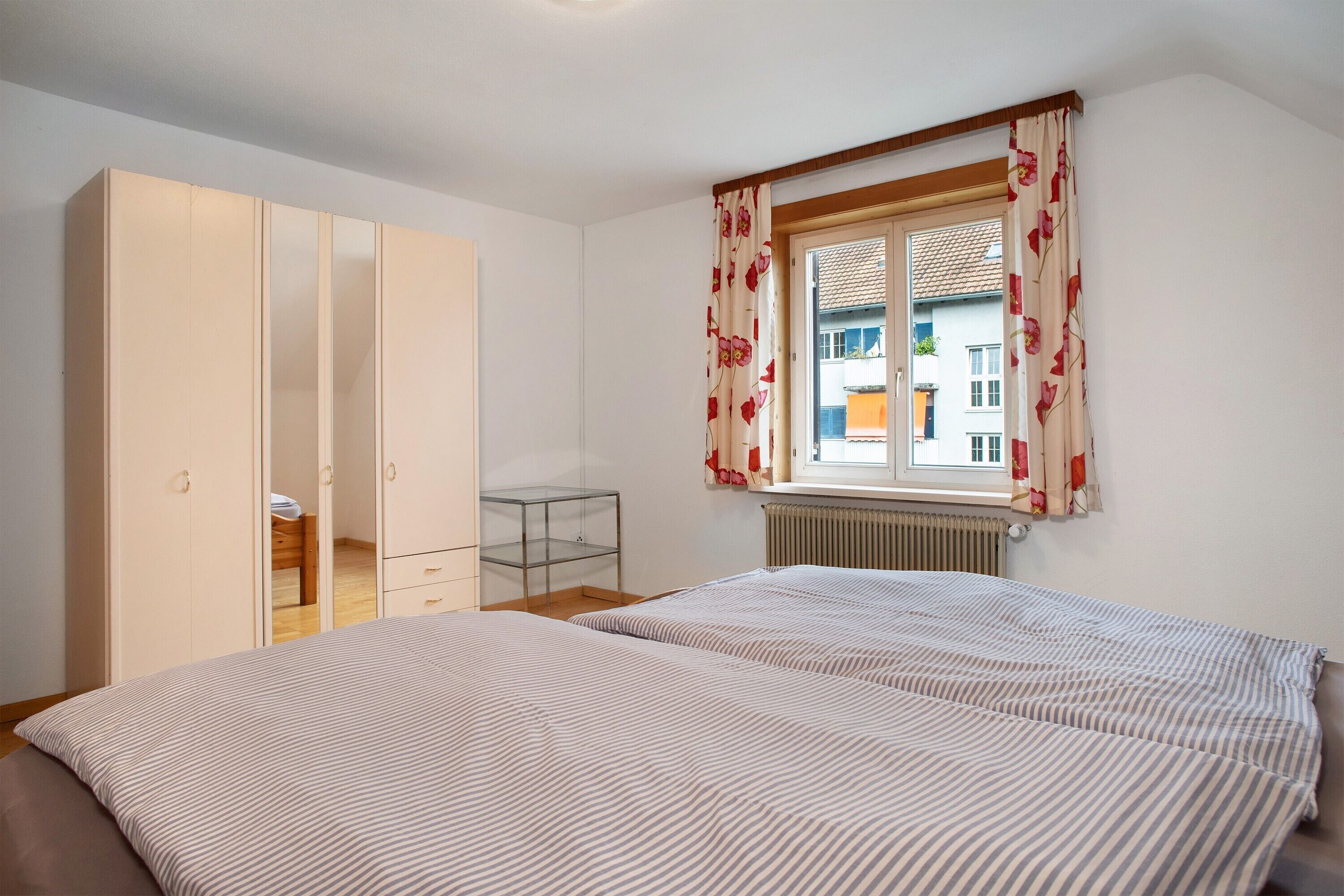 A bedroom with a bed, wardrobe, and a window with curtains.