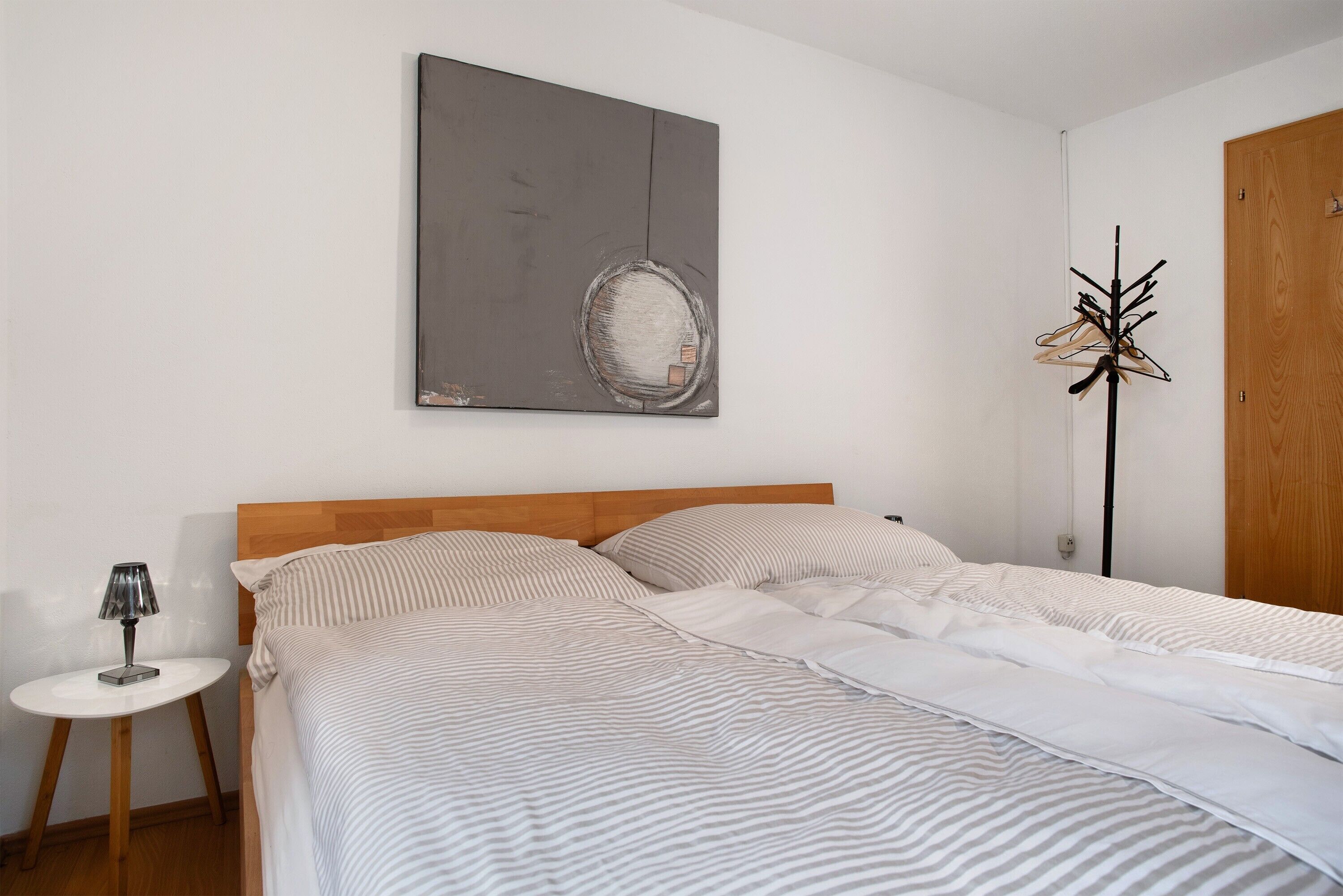 A bedroom with a bed, a round table, a coat rack, and a wooden door.