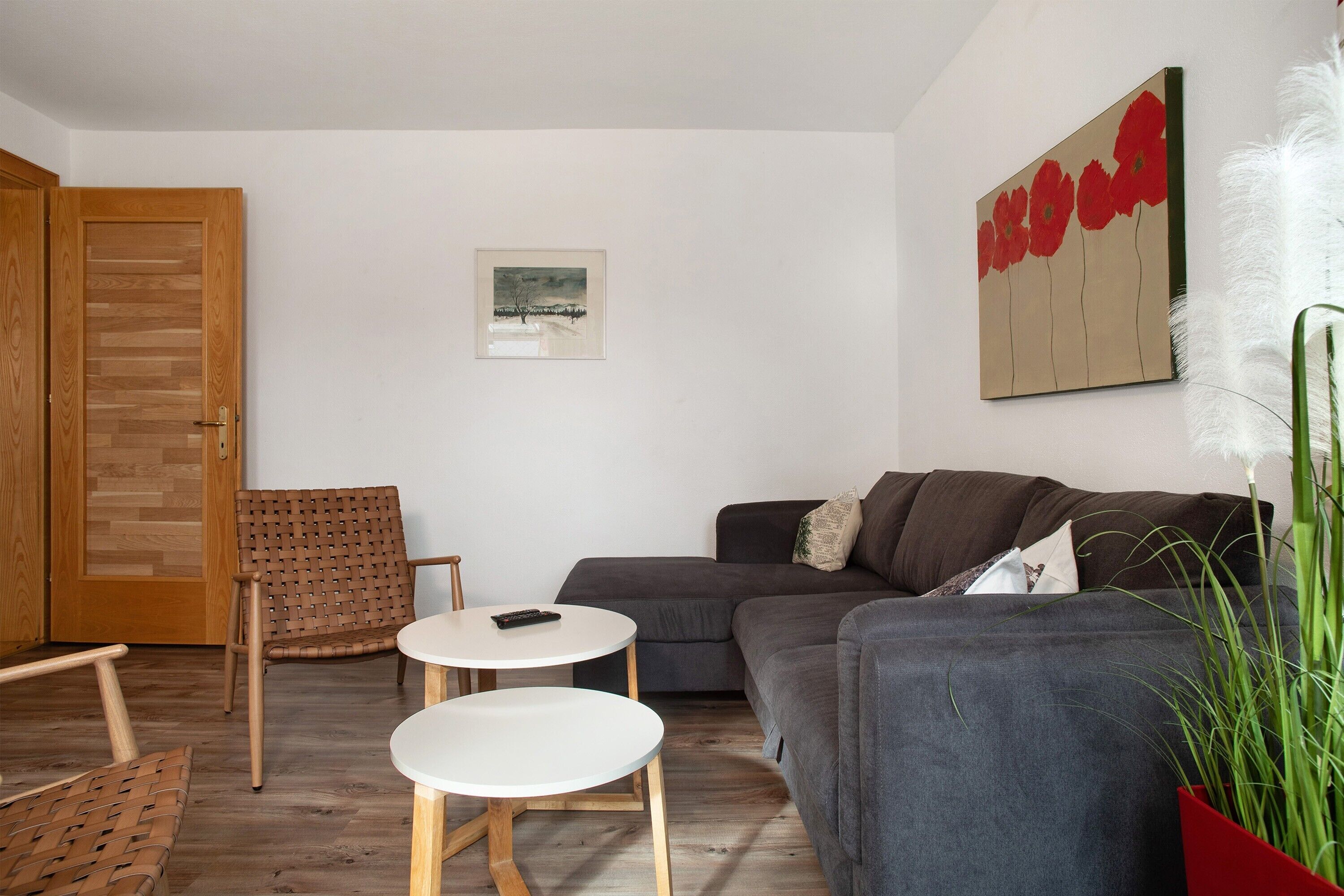 Ein Wohnzimmer mit einer Couch, zwei runden Tischen, einer Holztür und einem Gemälde an der Wand.