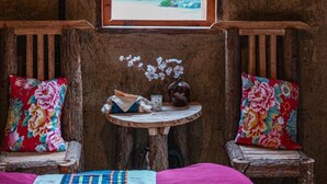 A rustic room with a wooden bench, a small round table with a vase, and a framed picture of a garden scene. - Long Co Tran Homestay (Lung Cu)