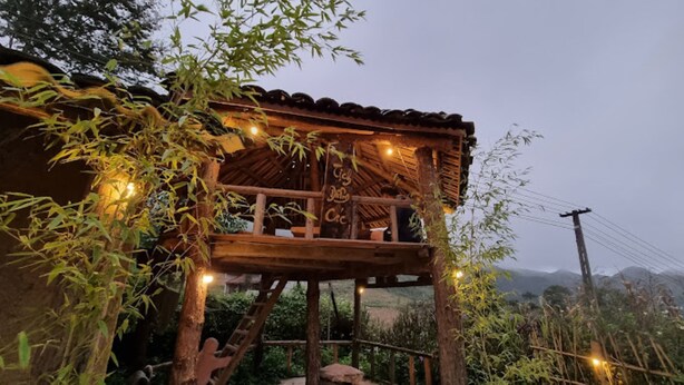 A wooden structure with a balcony, surrounded by bamboo and illuminated by string lights. - Long Co Tran Homestay (Lung Cu)