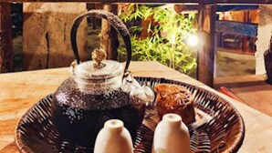 A wicker basket with a teapot and sugar cubes on a wooden table, set outdoors at night with bamboo plants in the background. - Long Co Tran Homestay (Lung Cu)