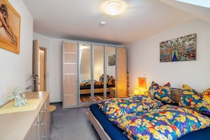 A bedroom with a bed, a wardrobe, a desk, and a painting on the wall.