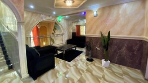 Eine großzügige Lobby mit Marmorboden, einer Treppe, einem schwarzen Sofa und einer Topfpflanze.