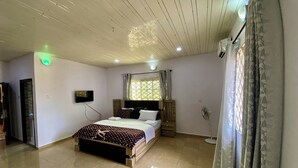 Ein Schlafzimmer mit einem Bett, einem Fernseher, einem Fenster mit Vorhängen, einem Ventilator und einer Tür.