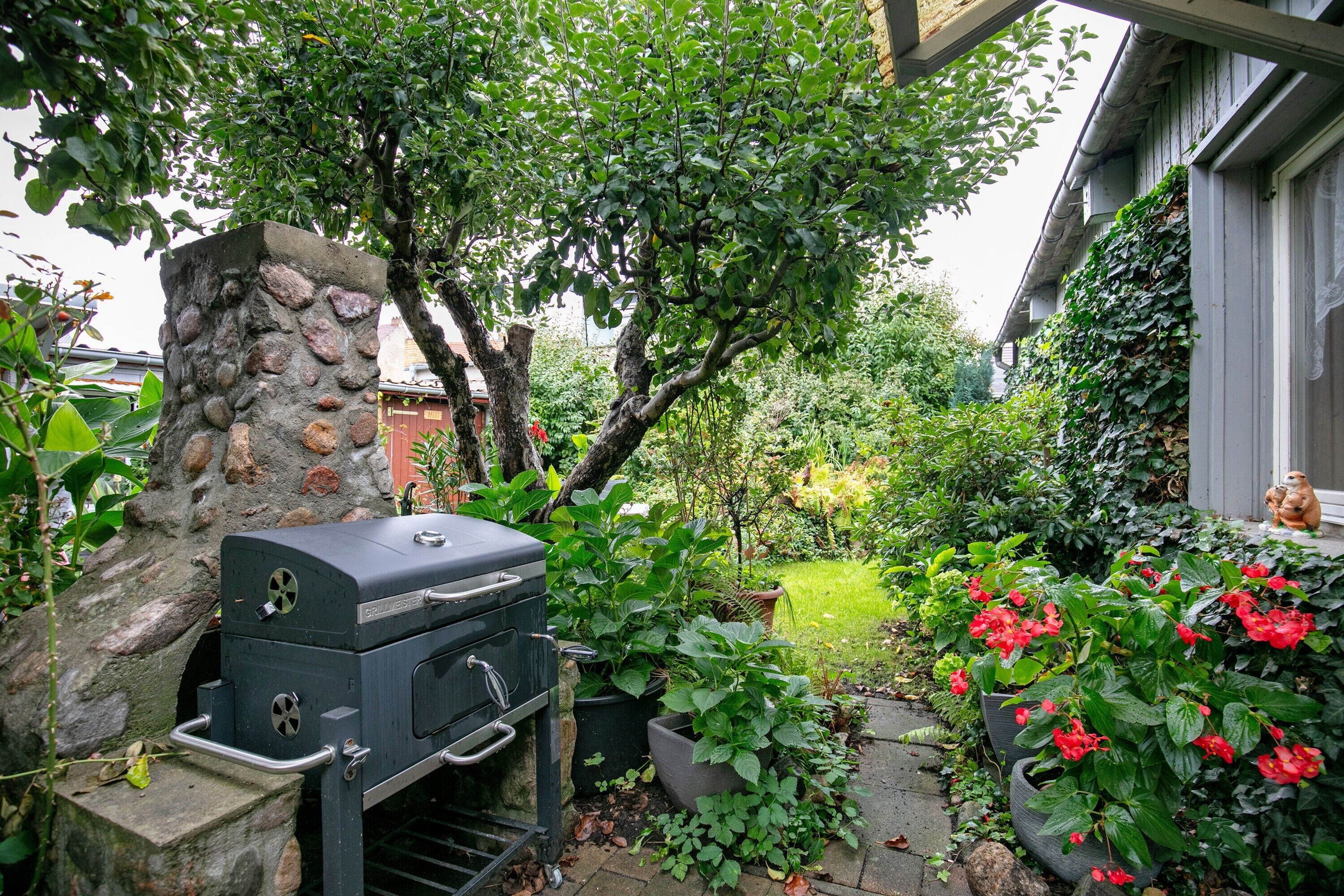 Ein Steingrill, Kübelpflanzen und ein Garten mit roten Blüten.