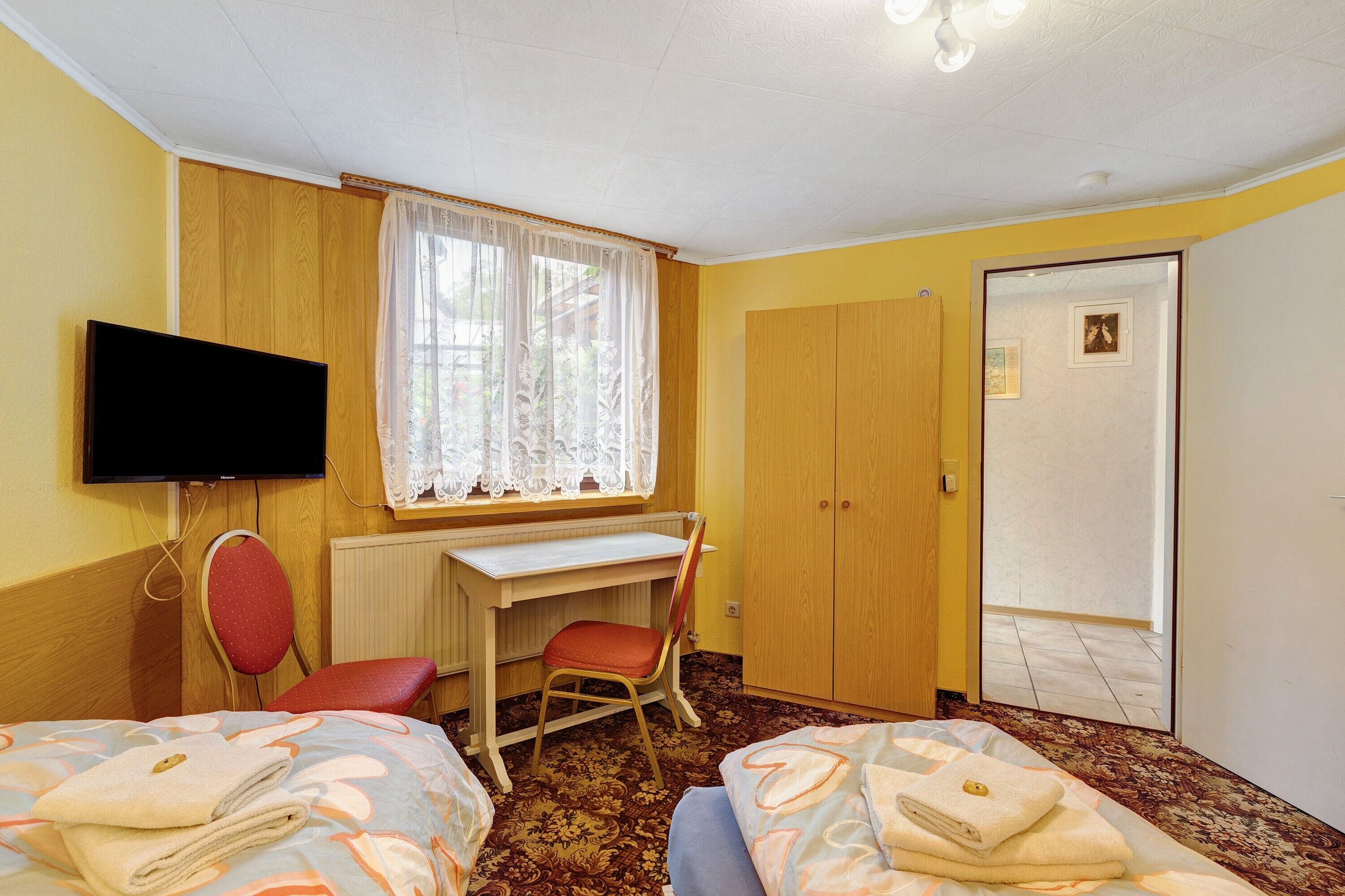 A room with two beds, a desk, a chair, a television, and a wardrobe.