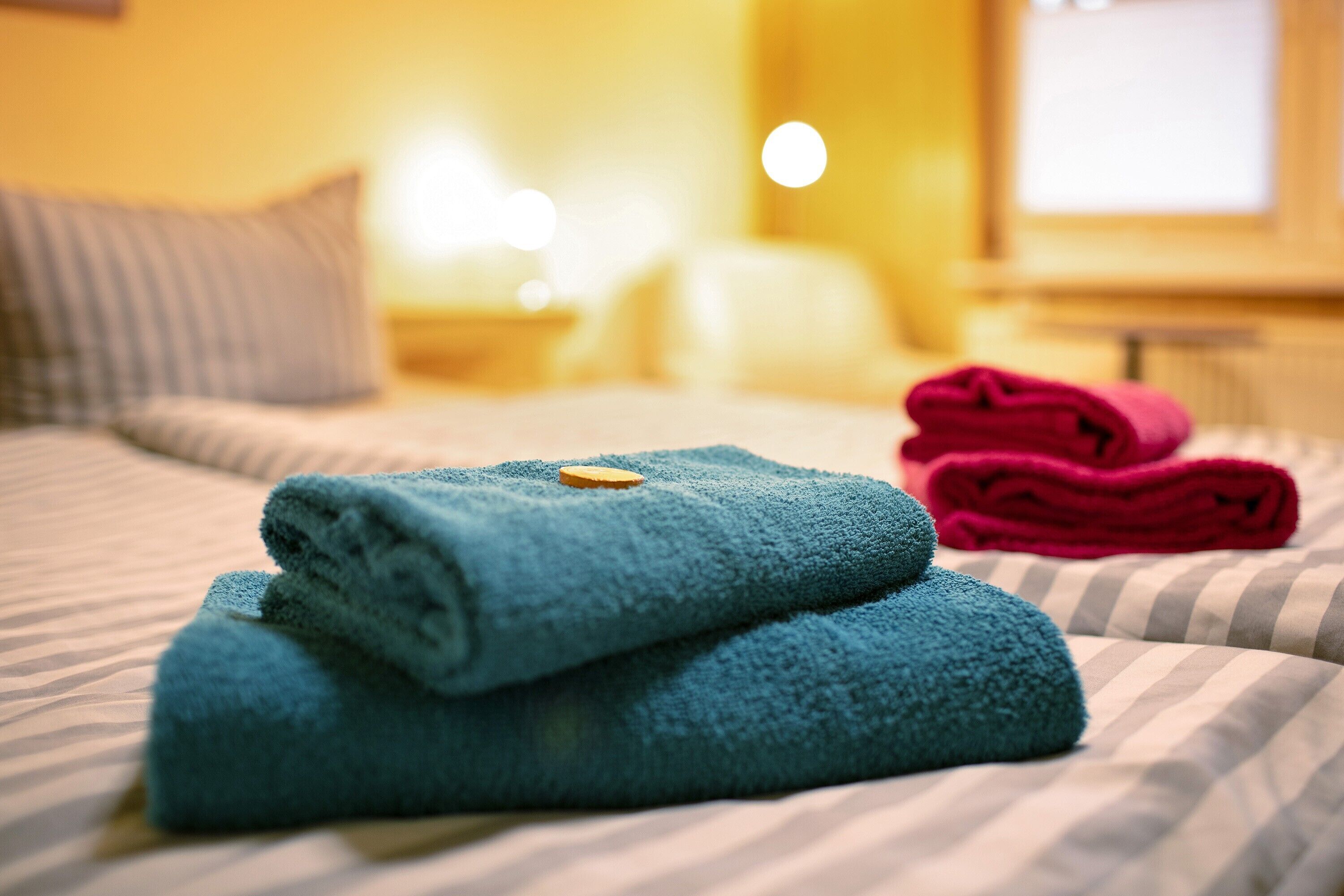 A bed with striped bedding, a blue towel, and a red towel.