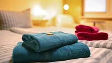A bed with striped bedding, a blue towel, and a red towel.