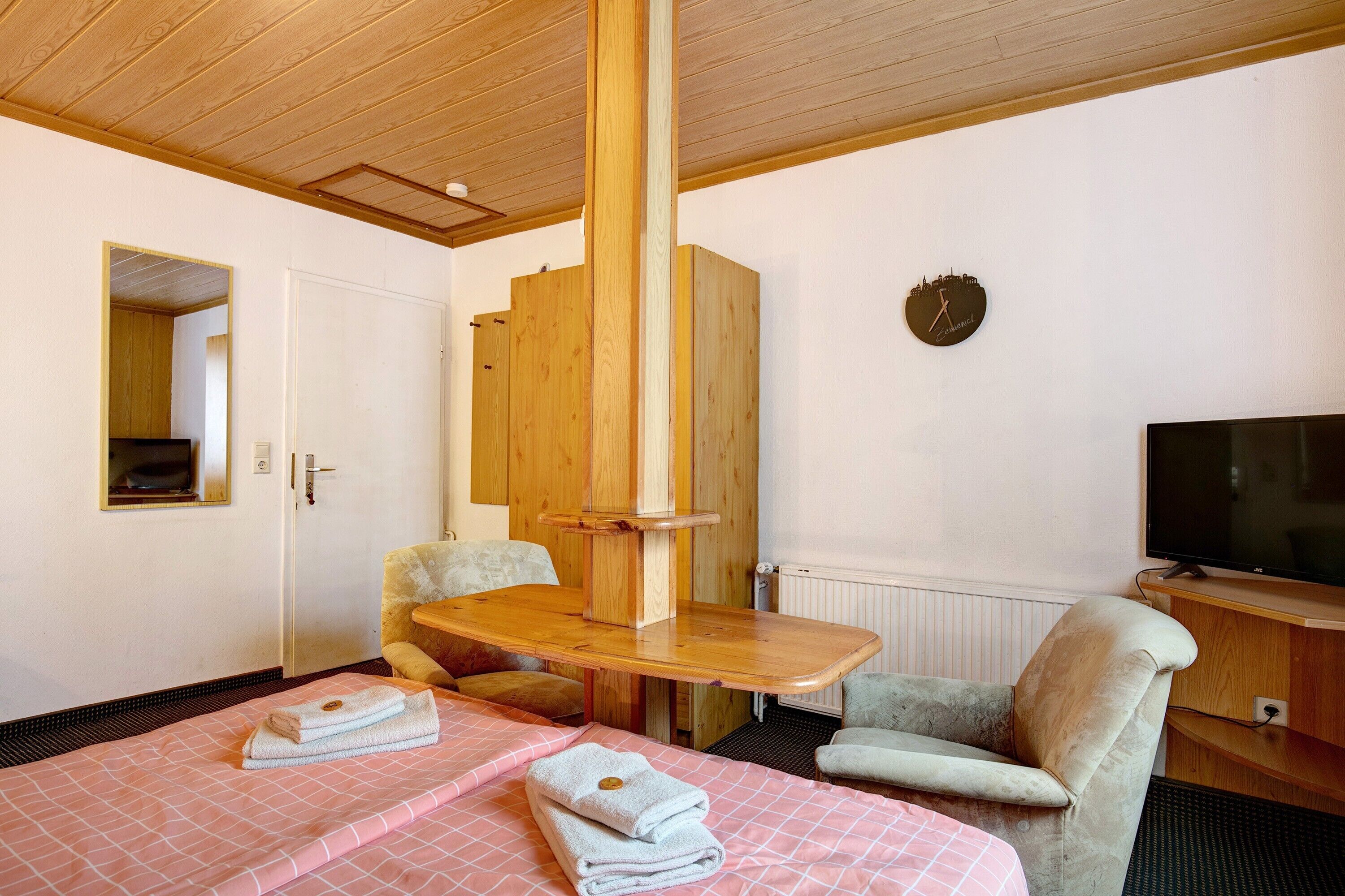 Una habitación de hotel con dos camas, una mesa de madera, un televisor y un espejo.