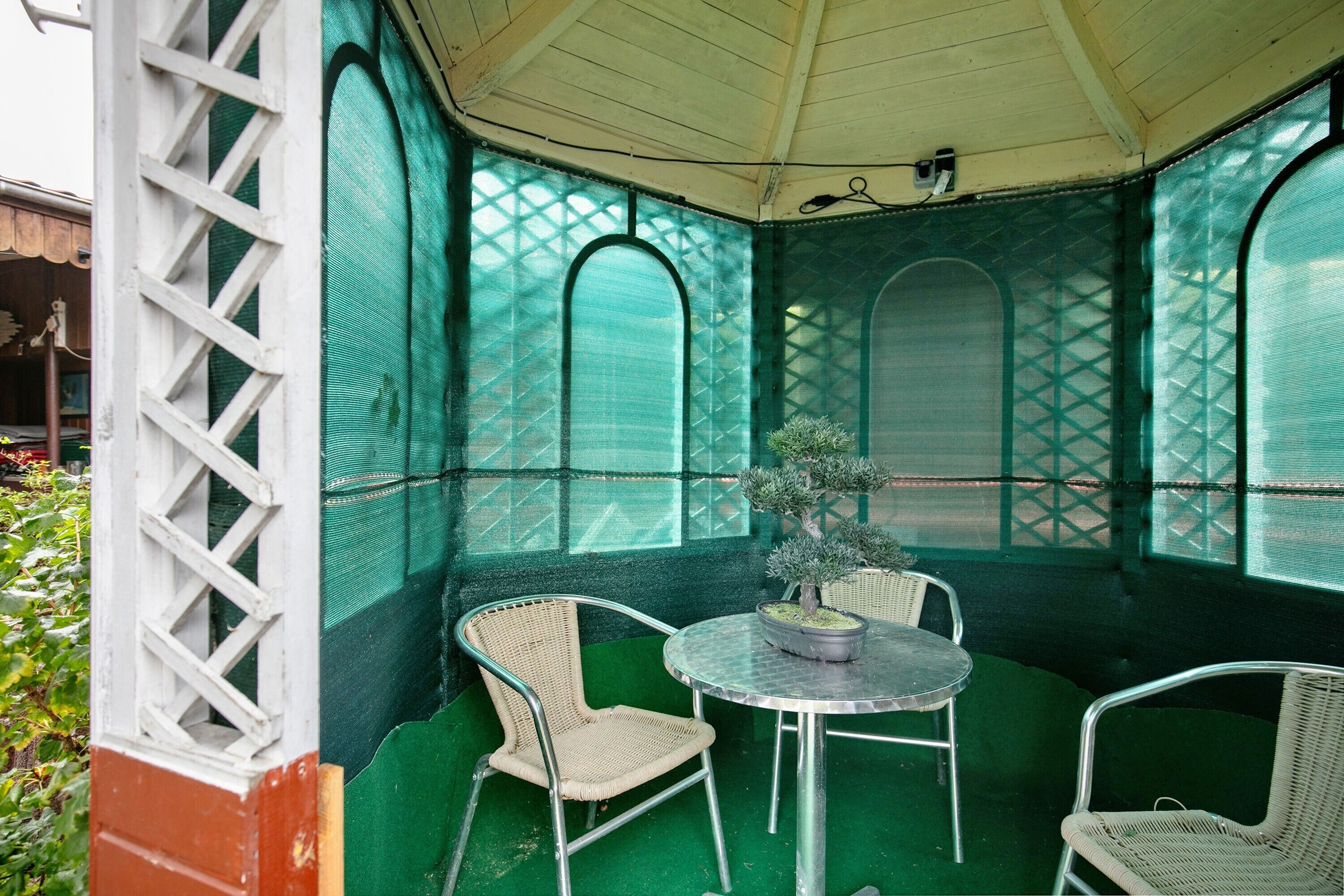 Une terrasse couverte avec une table et des chaises, une plante en pot et une fenêtre à treillis.