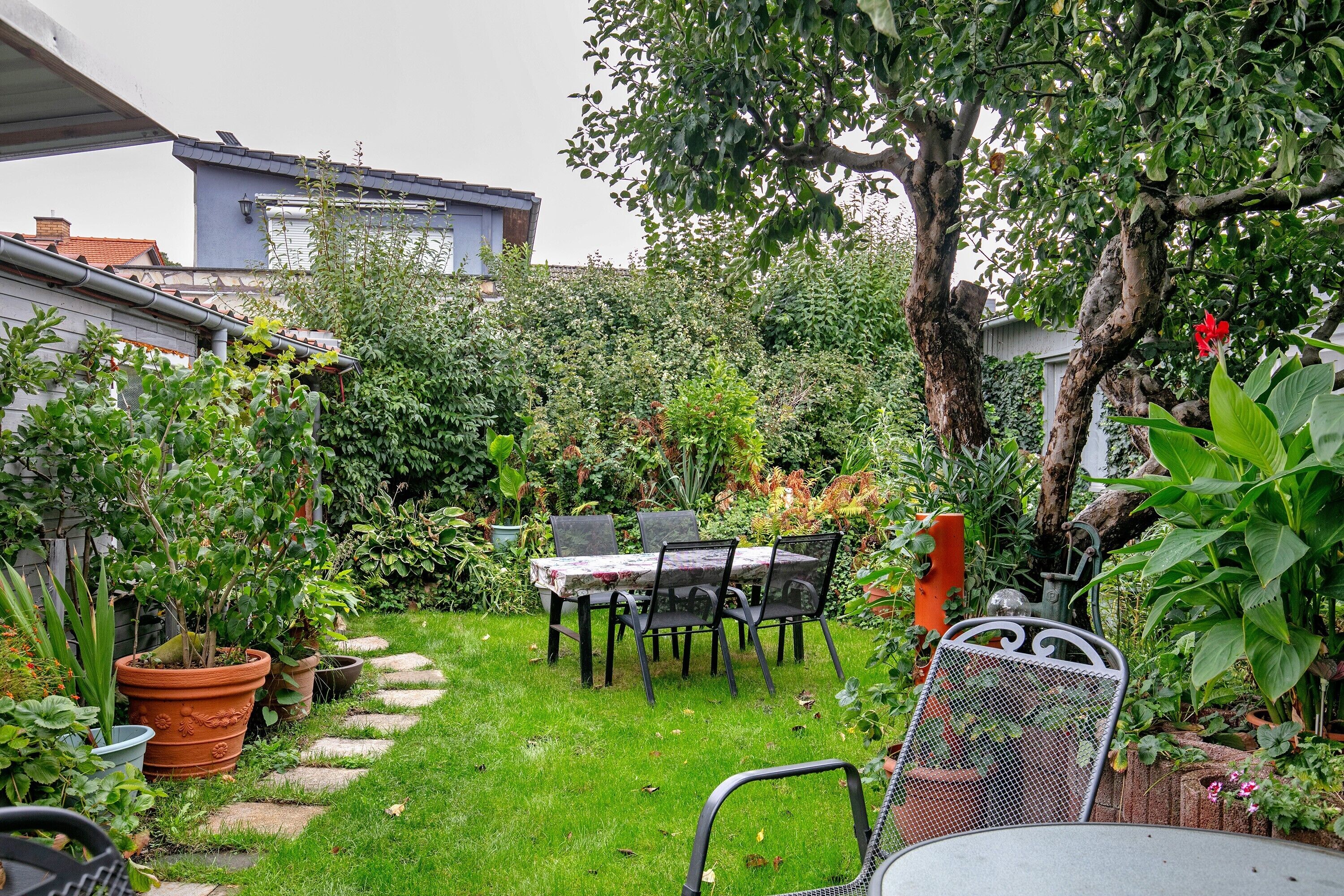 A garden with a table and chairs, surrounded by potted plants and a tree.