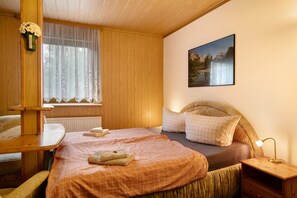 Une pièce aux murs lambrés, comprenant un lit, un bureau, une chaise, une fenêtre avec des rideaux légers et un tableau accroché au mur.