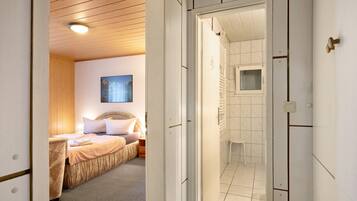 Un dormitorio con cama, mesita de noche, ventana y baño con ducha e inodoro.