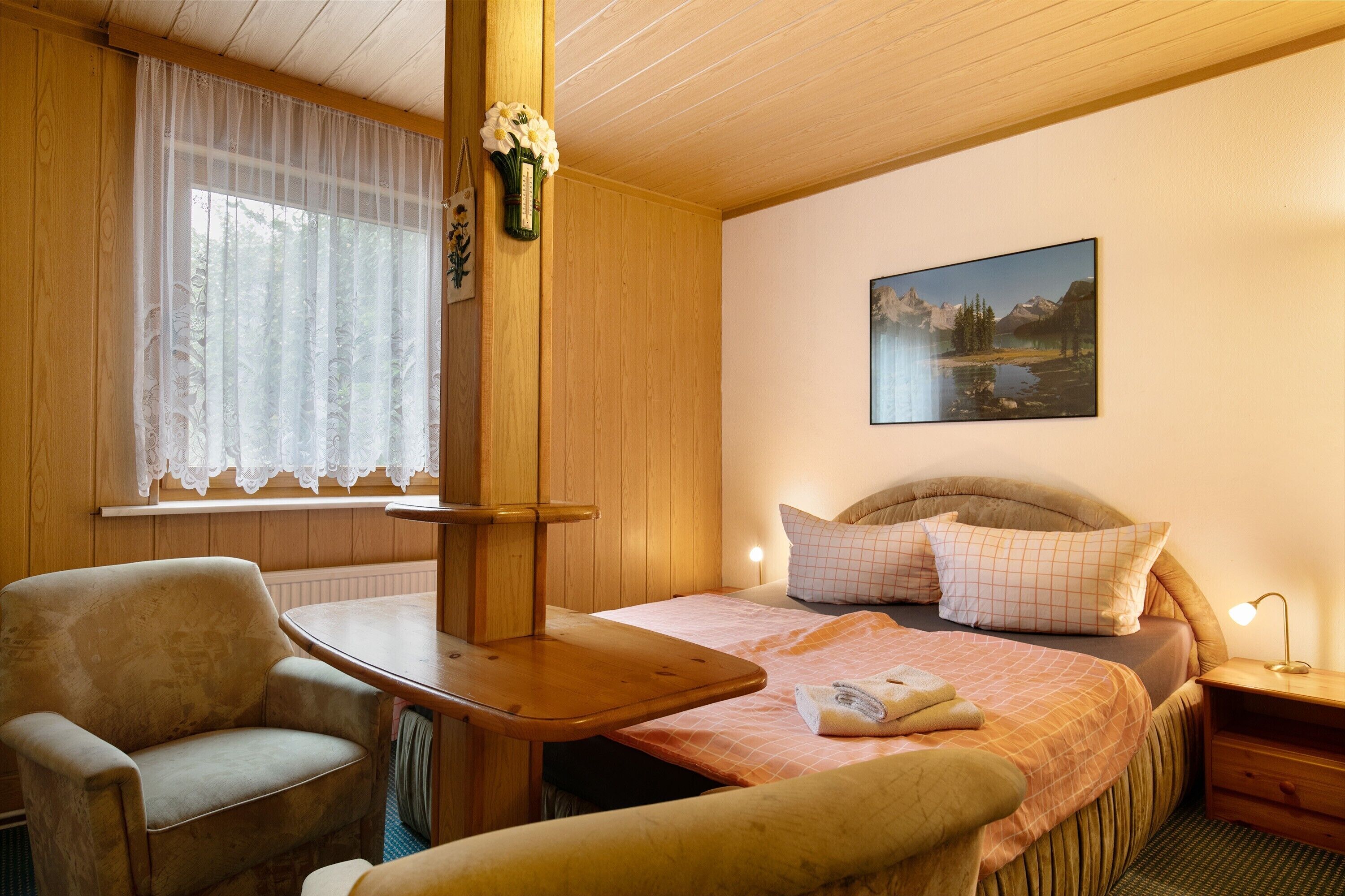 Une pièce confortable avec un lit, une chaise, une table et un tableau accroché au mur.