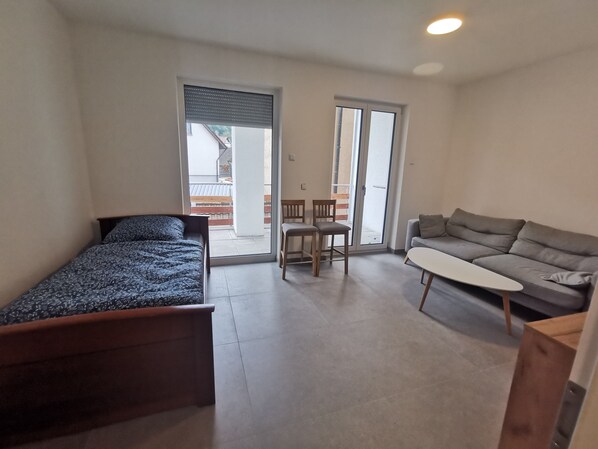Une petite chambre moderne comprenant un lit, un canapé, une table et une porte-fenêtre coulissante donnant sur un espace extérieur.