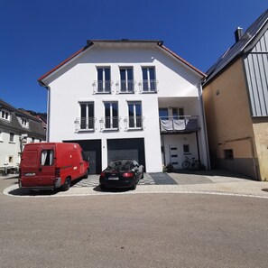 Un immeuble de deux étages avec un garage, un camion rouge et une voiture noire garés devant.