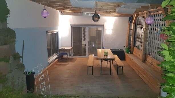 Un pati amb una taula i bancs de fusta, una porta corredissa de vidre i una tanca de fusta.