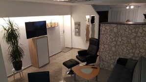 Un saló modern amb televisió de pantalla plana, una paret d'accent de pedra, una cadira d'oficina negra, un sofà gris i una planta en test.