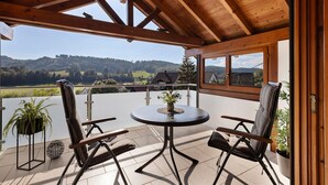 Um espaço ao ar livre coberto com uma mesa, cadeiras, um vaso de planta e vista para uma paisagem montanhosa.