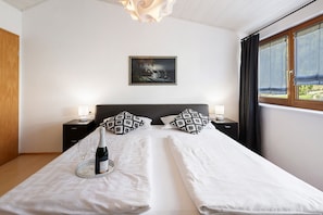 Un lit double avec du linge de lit blanc, deux coussins à motifs, une bouteille de champagne et deux verres sur un plateau.
