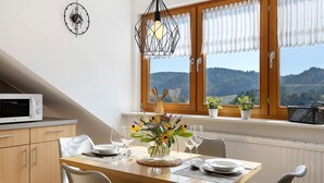 Uma sala de jantar com uma mesa posta para dois, micro-ondas, relógio e vista para o exterior.