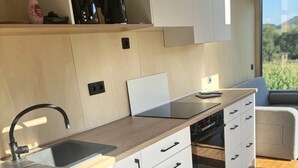 A modern kitchen with a sink, stove, and cabinets, a window with a view of greenery, and a wooden countertop. - Tiny Home 'Zuhause Im Freien' with Air Conditioning (Stockach)