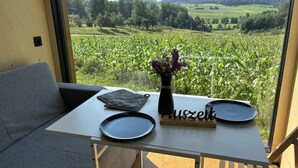A balcony with a table, a vase with flowers, and a view of a green field. - Tiny Home 'Zuhause Im Freien' with Air Conditioning (Stockach)