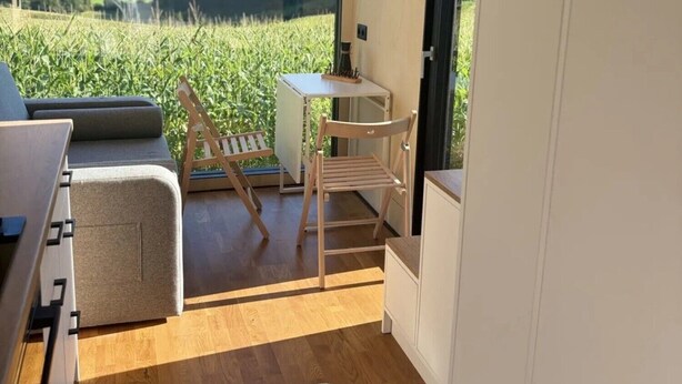 A compact kitchen with a large window, wooden flooring, and a view of a green field. - Tiny Home 'Zuhause Im Freien' with Air Conditioning (Stockach)