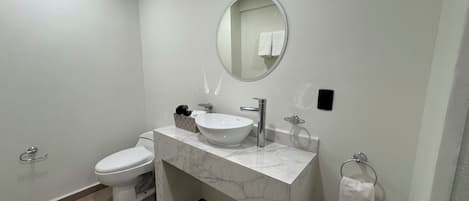 Un baño moderno con inodoro blanco, lavamanos de mármol y un espejo redondo.