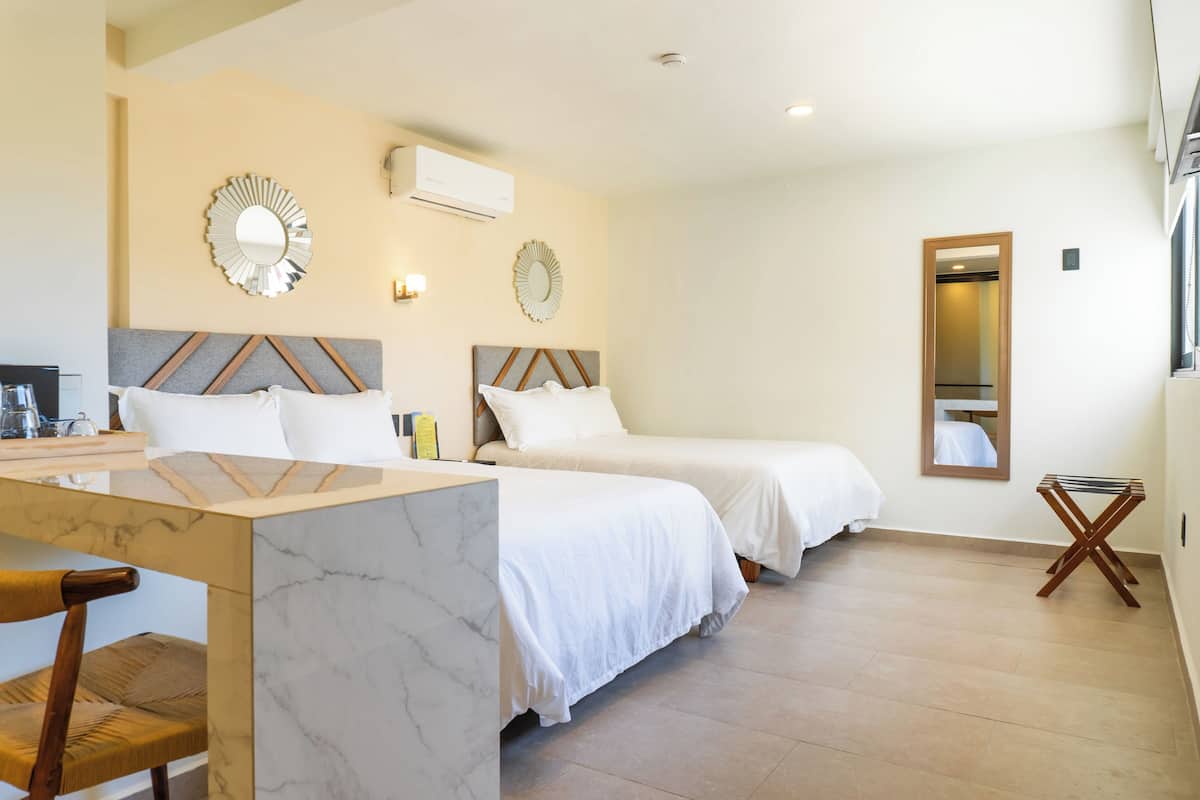 A hotel room with two beds, a marble desk, a wooden chair, and a small table.