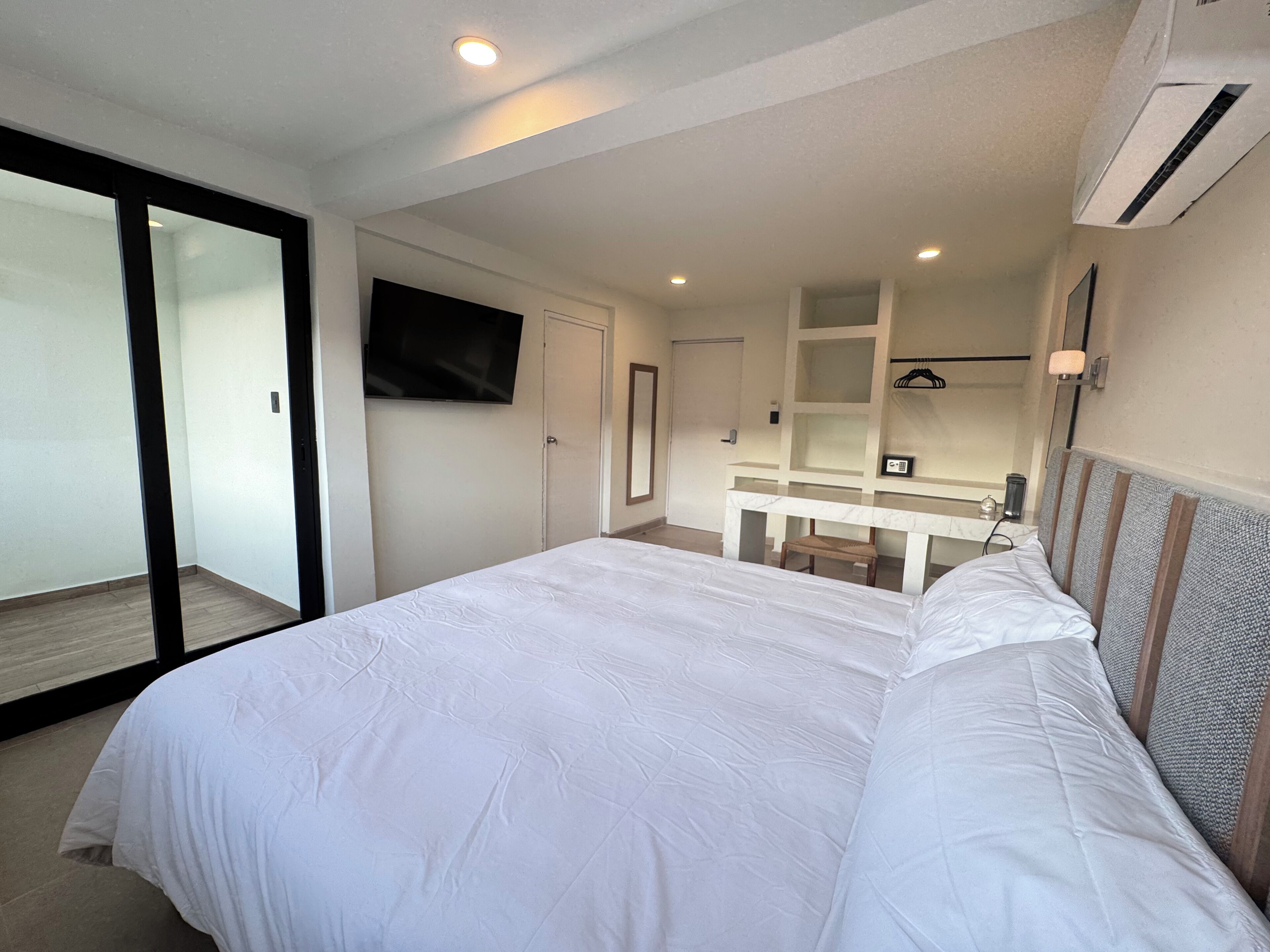 Una habitación de hotel moderna con una cama grande, un televisor montado en la pared, un escritorio pequeño y un espejo.