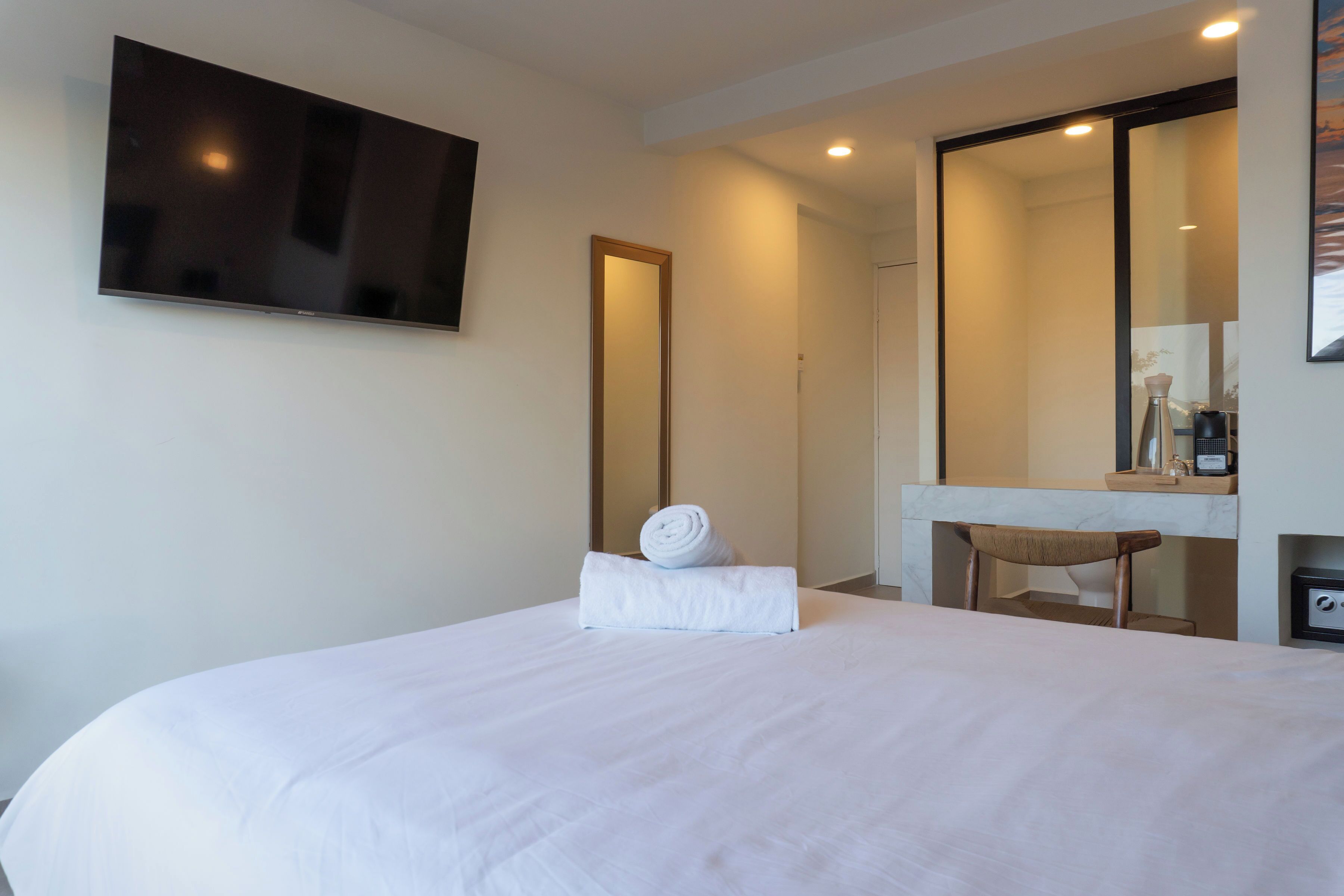 Hotelkamer met een bed, een aan de muur bevestigde televisie, een spiegel en een klein tafeltje met een stoel.