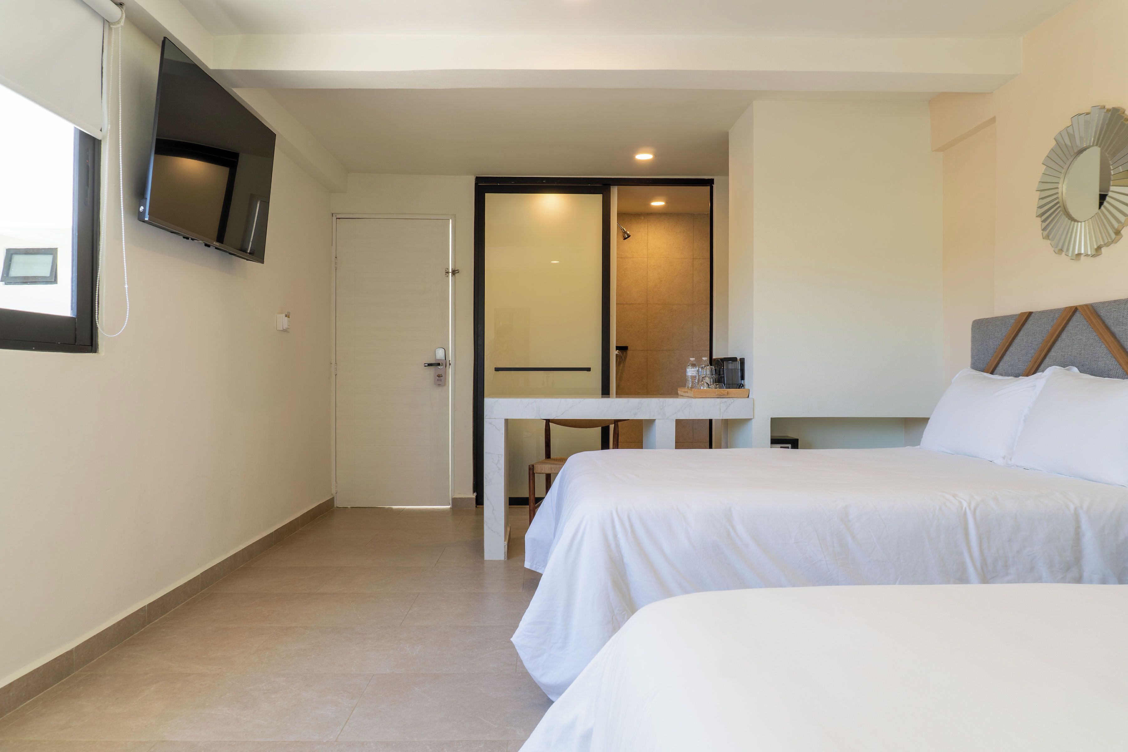 Ein Hotelzimmer mit zwei Betten, einem an der Wand befestigten Fernseher, einem kleinen Tisch und einer Tür zu einem Badezimmer.