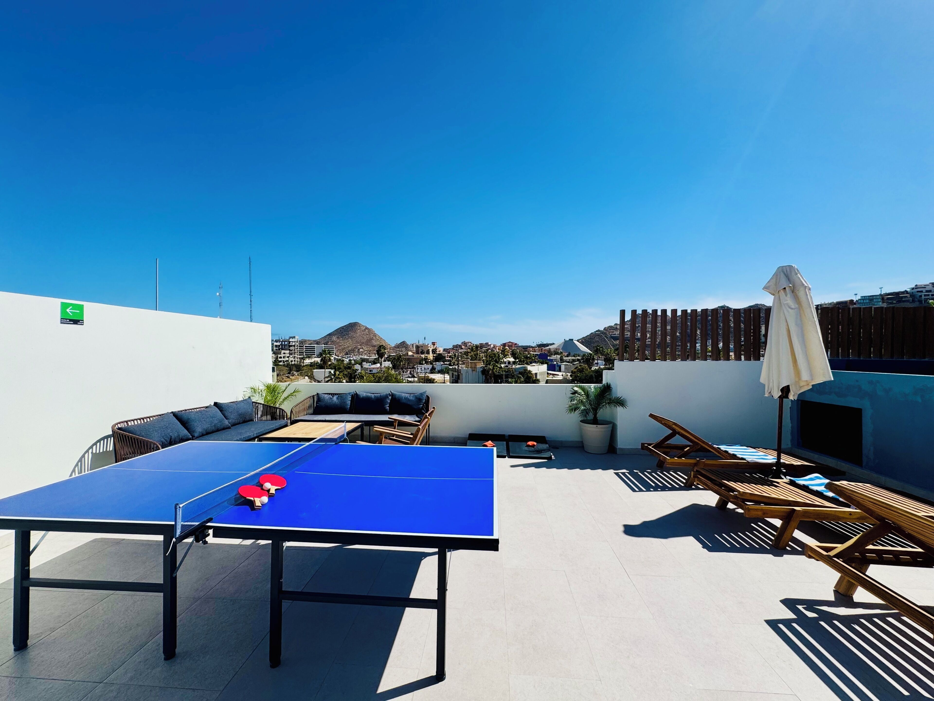 Eine Dachterrasse mit Tischtennisplatte, Liegestühlen und Blick auf die Stadt.