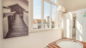 A room with a wooden table, a large window, and a wall-mounted picture of a wooden structure. - GuestReady - One prime stay in Lisbon (Lisbon)