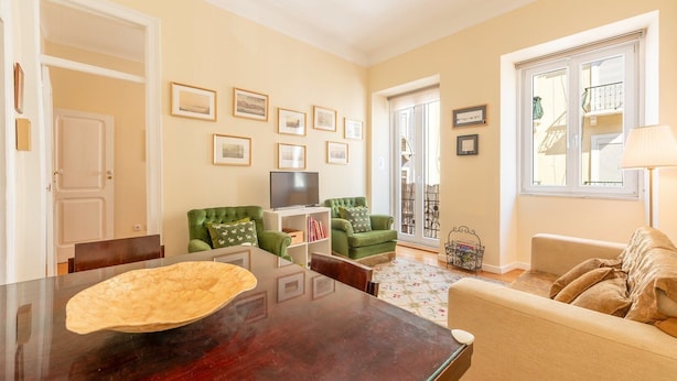A living room with a TV, green armchairs, a beige sofa, and a dining table. - GuestReady - One prime stay in Lisbon (Lisbon)