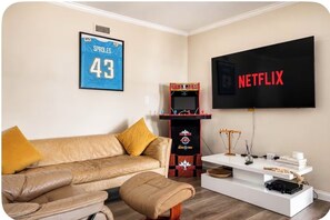 A living room with a sofa, ottoman, a basketball arcade machine, a TV, and a white console table.